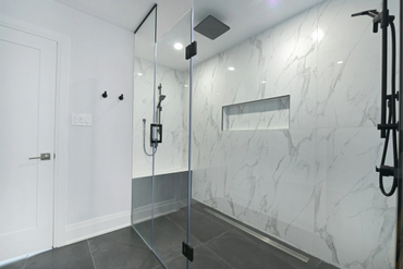 Modern shower with glass door and marble walls.