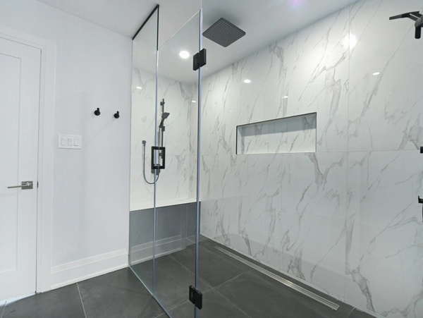 Modern shower with glass door and marble walls.
