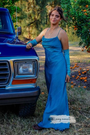 Young woman in blue dress posing by a vintage truck outdoors.