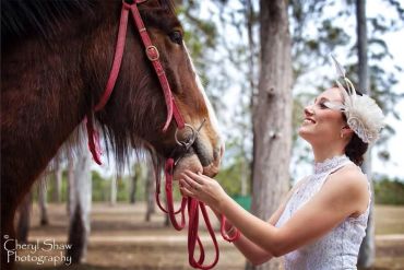 Woman smiling at a horse in a forest setting.
