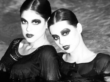 Two women with dramatic makeup and wet hair posing in water.