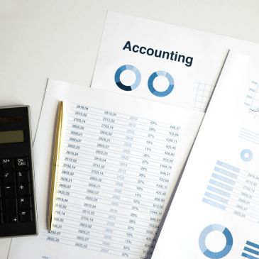 Accounting documents with graphs, table, calculator, and pen on desk.