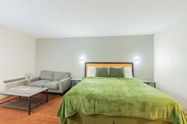 Simple hotel room with green bedding and gray sofa.
