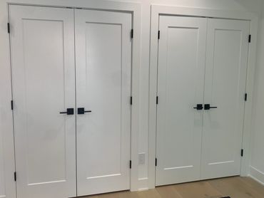 Two sets of white double doors with black handles inside a modern home.