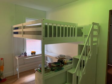 White loft bed with stairs and toys on a shelf beneath in a child's room.