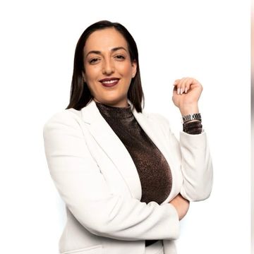 Confident woman in white blazer and dark top posing with a smile.