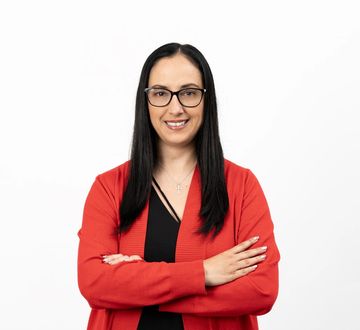 Confident woman with glasses and long hair wearing a red cardigan.