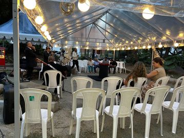 Concierto pequeño bajo toldo con sillas blancas y luces.