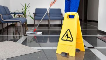 Mopping floor near caution sign.