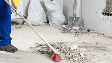 Worker sweeping construction debris floor.