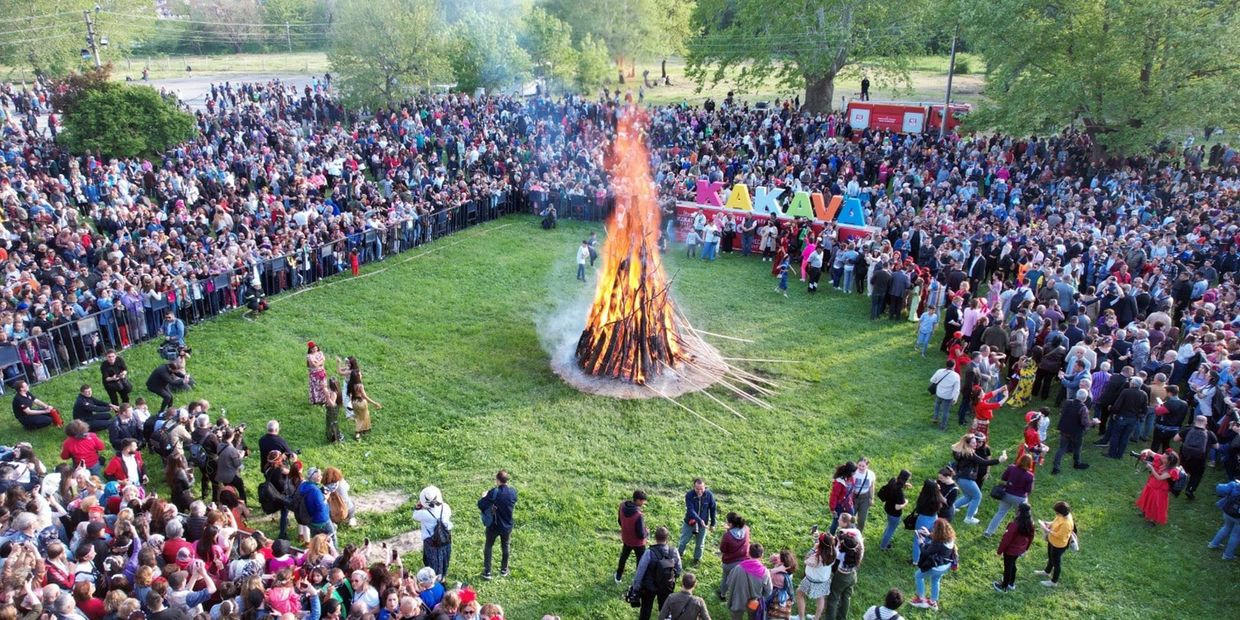 Crowd gathered around a large bonfire in a grassy park for a festival.