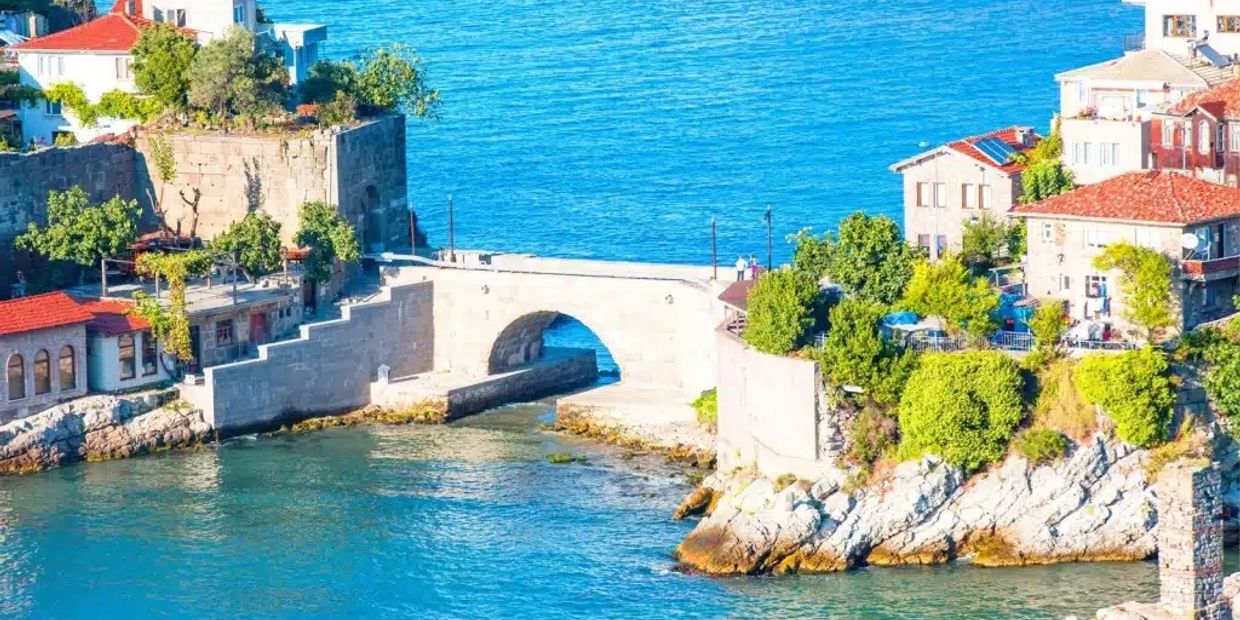 A scenic coastal village with stone buildings and a small arched bridge over blue water.
