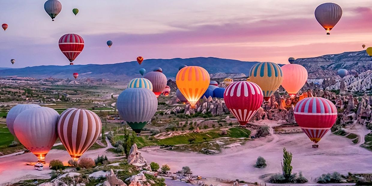 Colorful hot air balloons float over a scenic landscape at sunrise.