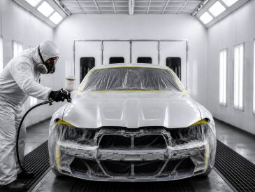 Technician spray painting a car in a booth.