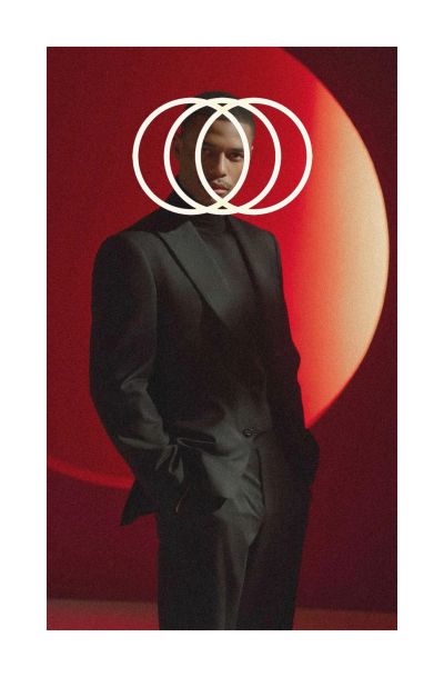 Un homme en costume noir devant un fond rouge avec des cercles blancs.
