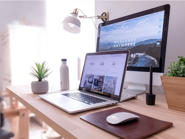 Modern workspace with laptop, desktop, and plants on a wooden desk.