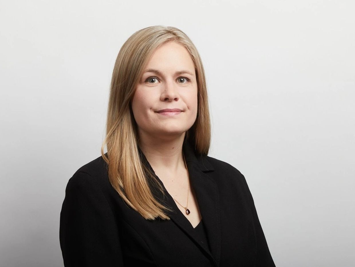 Professional woman in black blazer against white background.