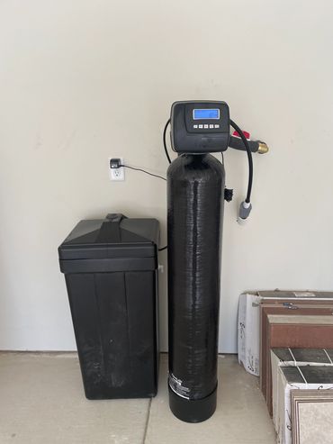A black water softener system installed against a beige wall.