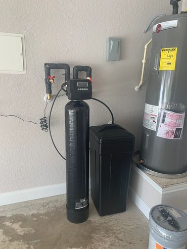 Water softener system installed next to a water heater in a utility room.