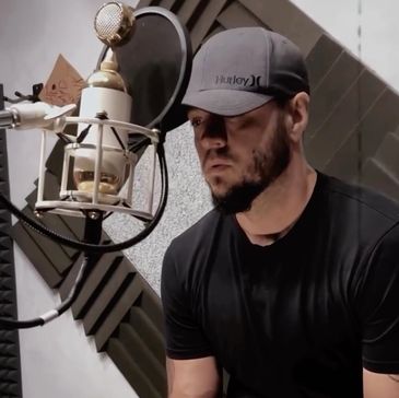 Man in a black shirt recording vocals in a studio.