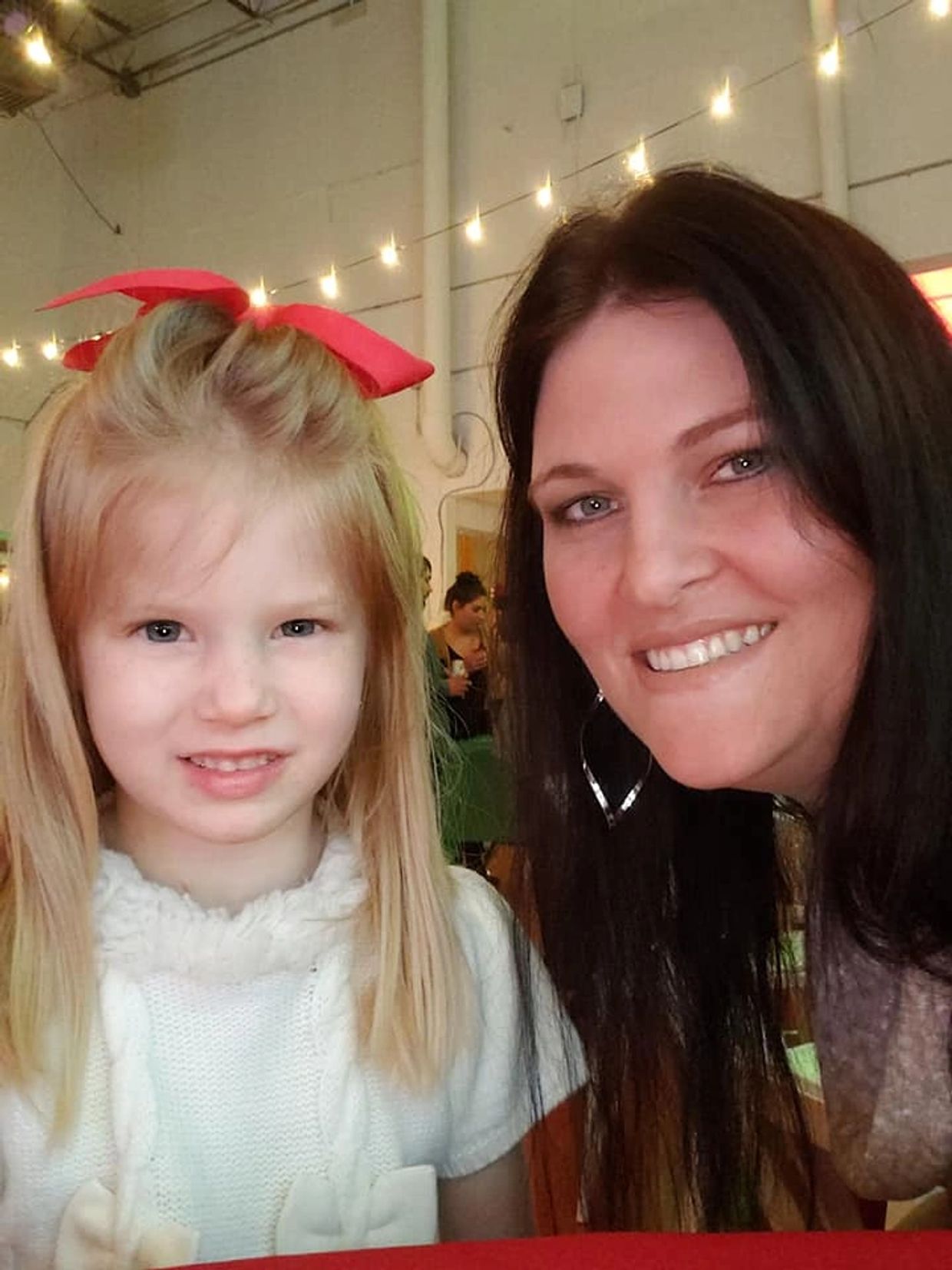 Smiling woman and young girl with a red bow in a warmly lit room.