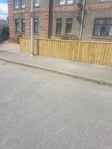 Residential street with a wooden fence and brick building under a sunny sky.