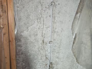 Cracked concrete wall with a plastic pipe and wooden frame.