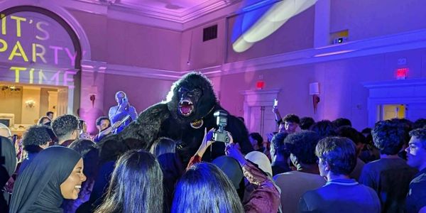 A lively party with a person in a gorilla costume entertaining a crowd indoors.