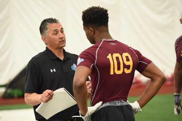 Coach talking to athlete wearing maroon jersey number 109 indoors.