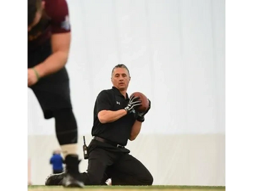 Man in black sportswear kneeling and holding a football on the field.