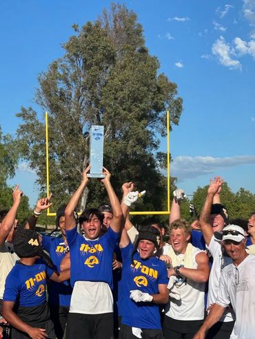 Youth football team celebrating a championship trophy outdoors.