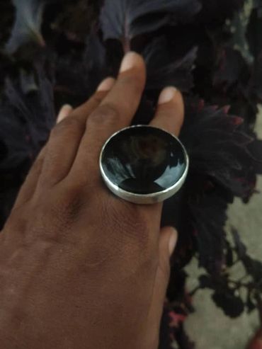 Hand wearing a large black oval ring against dark purple leaves.