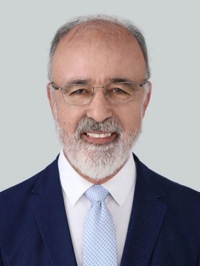Smiling elderly man in glasses and a suit with a light blue tie.