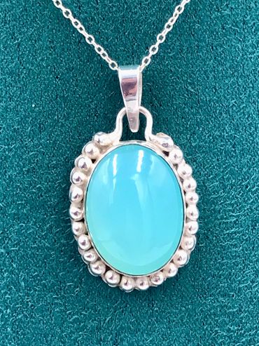 A silver pendent consisting of a bezel set oval blue chalcedony cabochon surrounded by granules of s