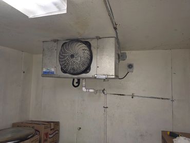 Ceiling-mounted industrial fan unit in a storage room with boxes.