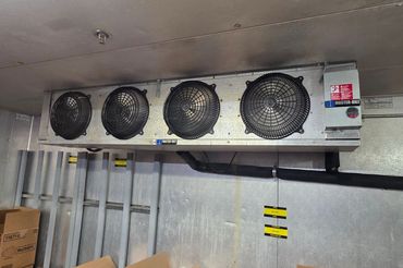 Industrial cooling fans mounted on a metal wall in a storage area.