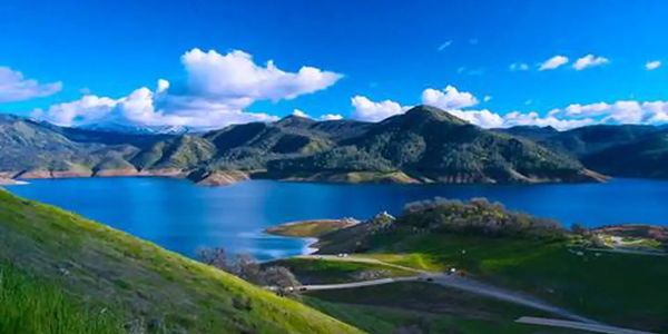 Scenic lake surrounded by green hills and mountains under a bright blue sky.