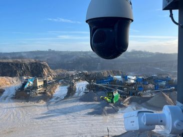 Surveillance cameras overlooking an industrial quarry site with machinery and piles of materials.