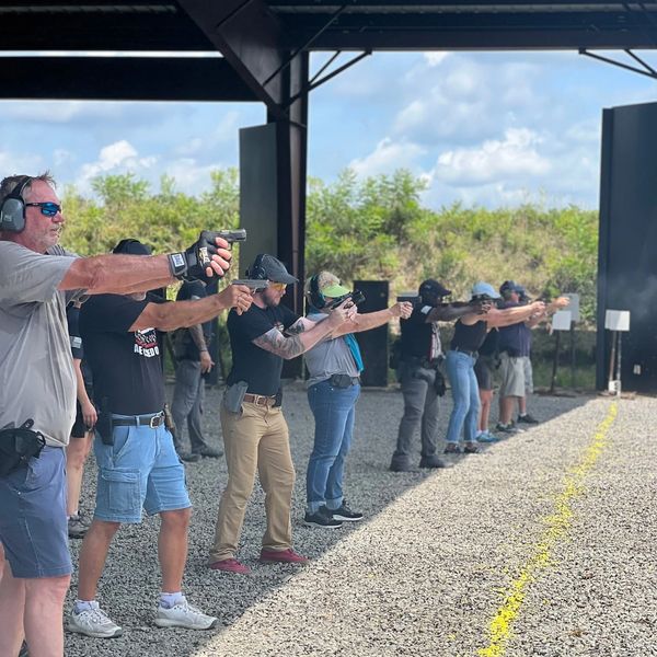 A group of people lined up at a shooting range practicing with handguns during Pistol Foundations 201.