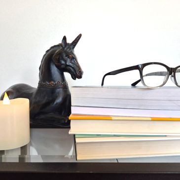 Black unicorn statue, candle, glasses, and stacked books on a glass table.