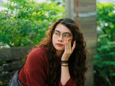 Thoughtful woman with glasses sitting on a bench outdoors.