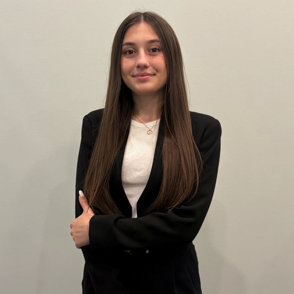 Young woman with long hair in black blazer smiles at camera.