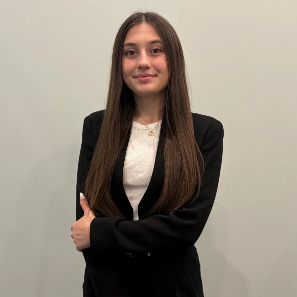 Young woman with long hair in black blazer smiles at camera.
