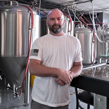 Man standing in a brewery with large fermentation tanks.