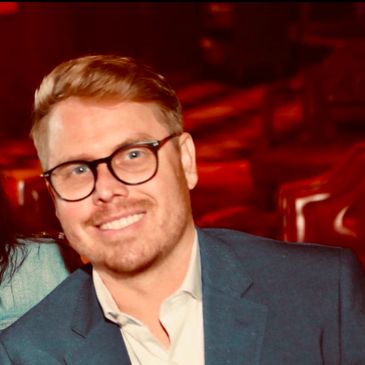 Smiling man with glasses in a suit jacket.