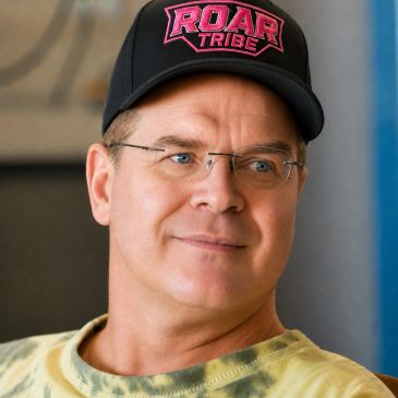 Man wearing glasses and a "ROAR TRIBE" cap.
