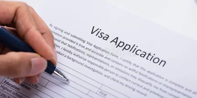Person filling out a visa application form with a pen.