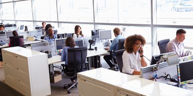 Modern office with employees working at desks and large windows.