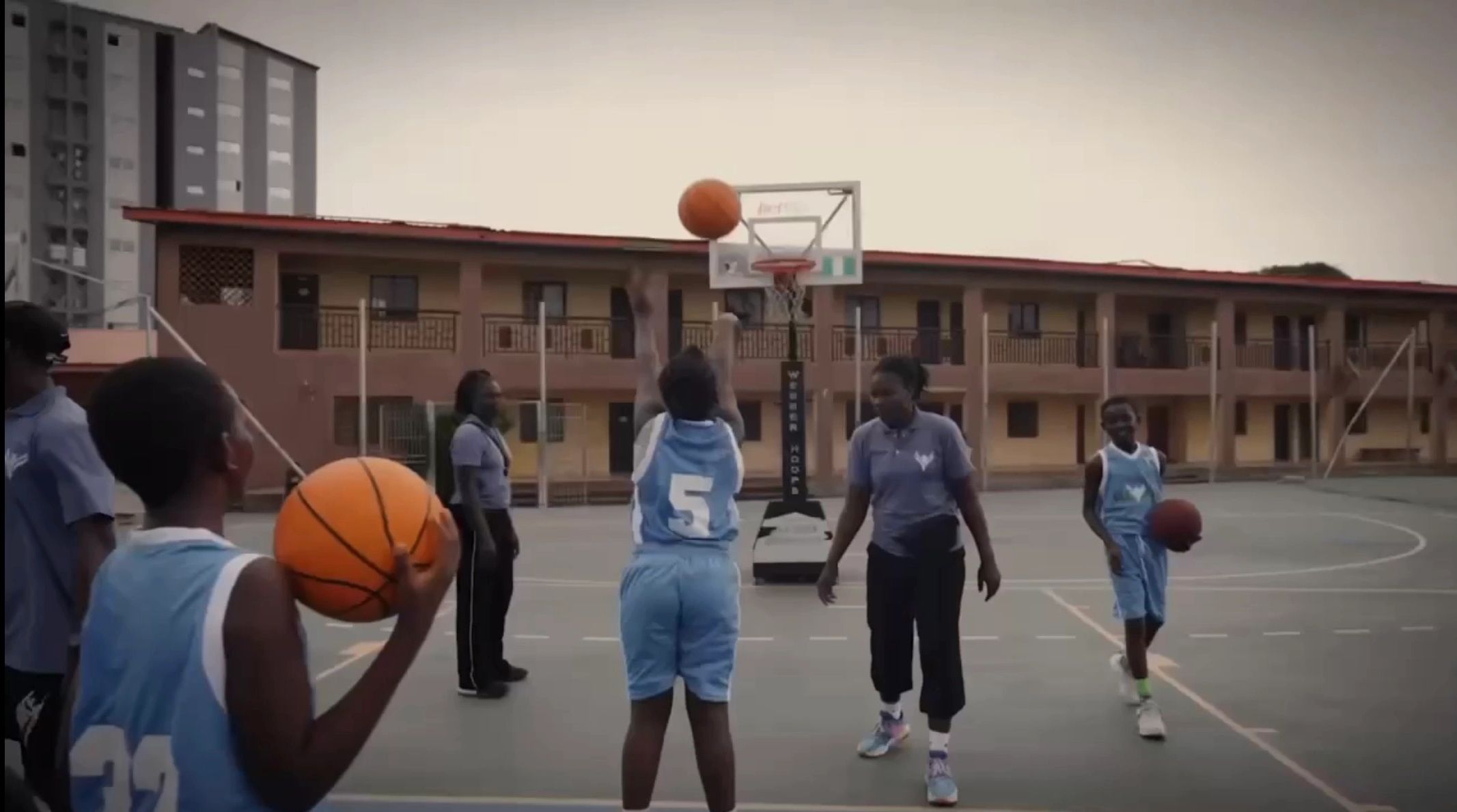 Children playing basketball on an outdoor court with coaches.