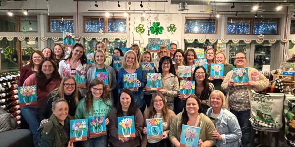 Group of women proudly displaying their flower paintings indoors.